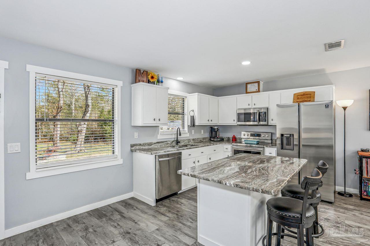 4010 Wyndham Road Century, FL 32535 - Photo 8 of 25 a kitchen with stainless steel appliances granite countertop a stove top oven a refrigerator a sink and white cabinets with wooden floor