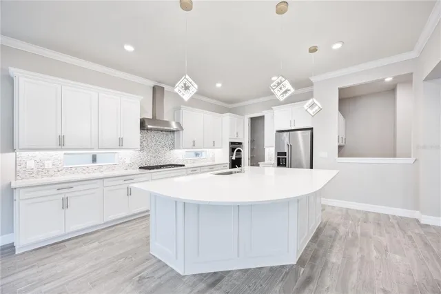 a large white kitchen with kitchen island a stove a sink a refrigerator and white cabinets with wooden floor