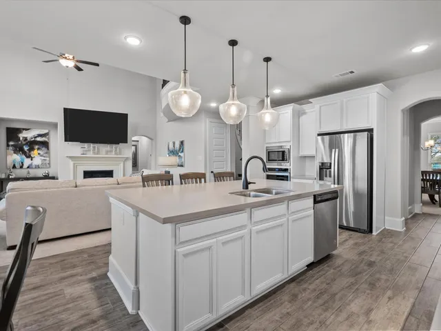 a large white kitchen with a sink stainless steel appliances and a chandelier