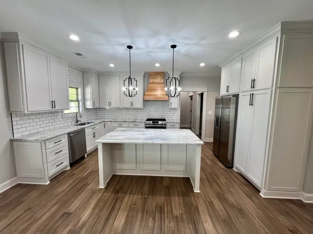 a large kitchen with granite countertop a large stove a sink dishwasher a refrigerator and white cabinets with wooden floor