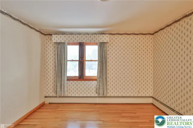a view of an empty room with a window and hardwood floor