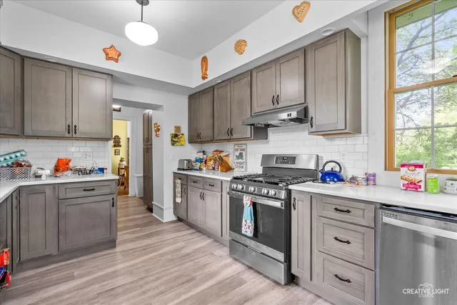 a kitchen with stainless steel appliances granite countertop a stove a sink dishwasher a refrigerator and white cabinets with wooden floor