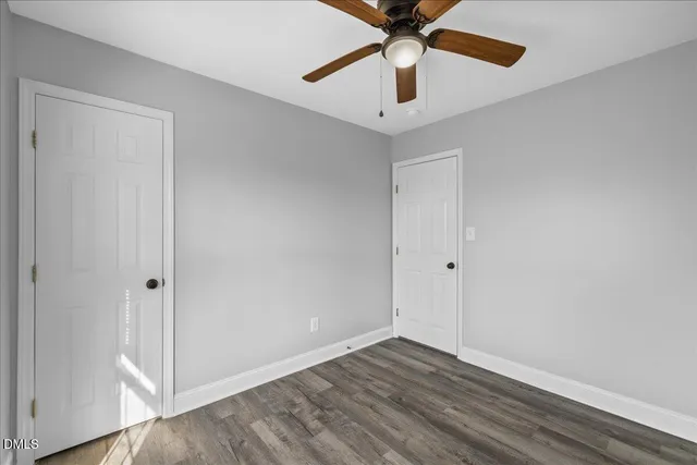 an empty room with wooden floor chandelier fan and windows