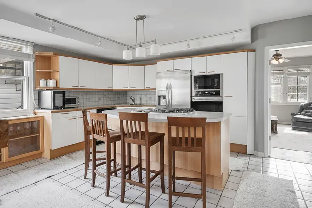 a kitchen with stainless steel appliances kitchen island granite countertop a dining table chairs and a refrigerator