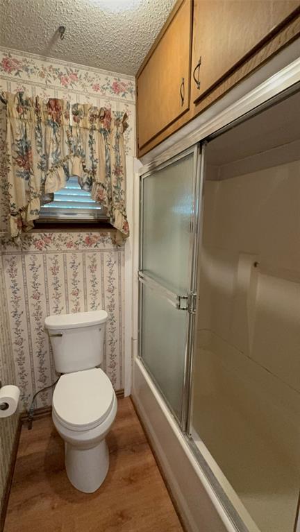 1387 Hickory Street Rhome, TX 76078 - Photo 15 of 36 Hallway bathroom. Wood-finish flooring with a toilet, a full bathtub with sliding frosted glass doors, and upper wood cabinetry.
