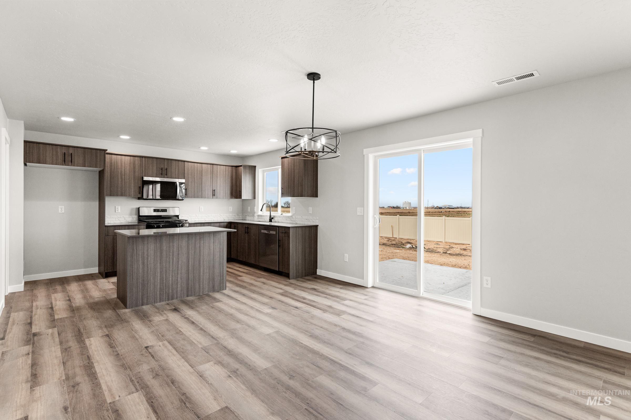 12830 Ropers Street Nampa, ID 83651 - Photo 7 of 18 Open-concept kitchen featuring wood-finish flooring, a central island, dark wood-finish cabinetry, stainless steel appliances, and a sliding glass door leading to an outdoor space