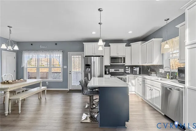a large kitchen with stainless steel appliances kitchen island granite countertop a large island a refrigerator a stove a sink a dining table and chairs with wooden floor