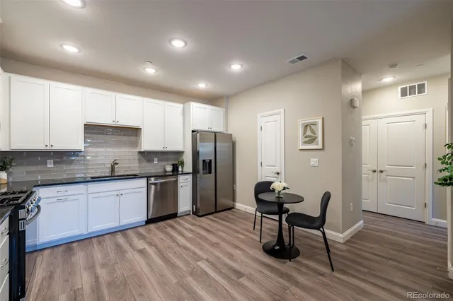 a kitchen with stainless steel appliances granite countertop a stove top oven a sink dishwasher and white cabinets with wooden floor