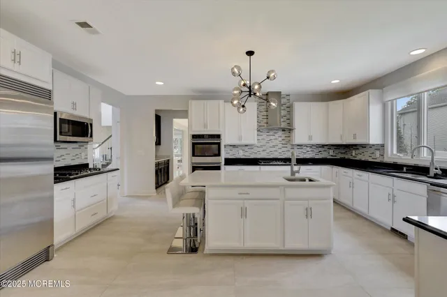 a open kitchen with stainless steel appliances granite countertop a stove a sink a refrigerator and white cabinets with wooden floor