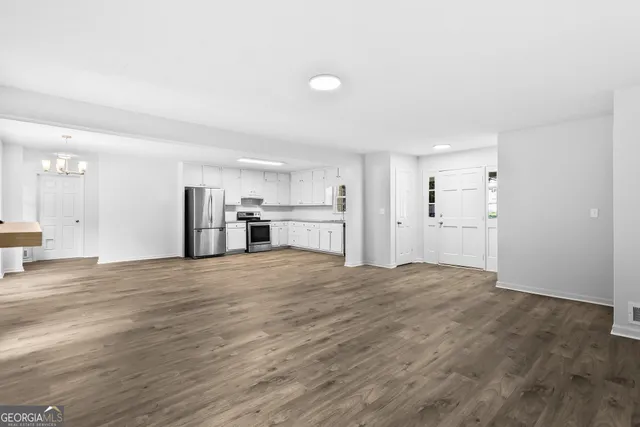 a view of empty room with wooden floor and kitchen