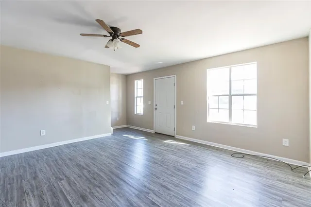 an empty room with wooden floor a ceiling fan and windows