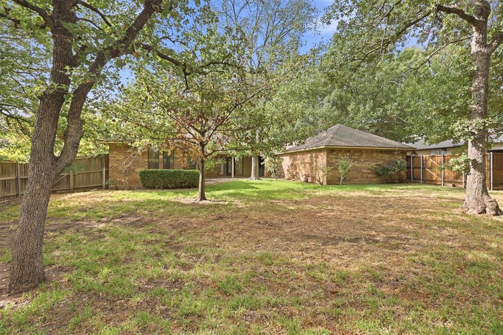 37 Timbergreen Circle Denton, TX 76205 - Photo 31 of 31 Expansive rear yard featuring mature trees, a brick-clad structure, and a wood fence enclosure