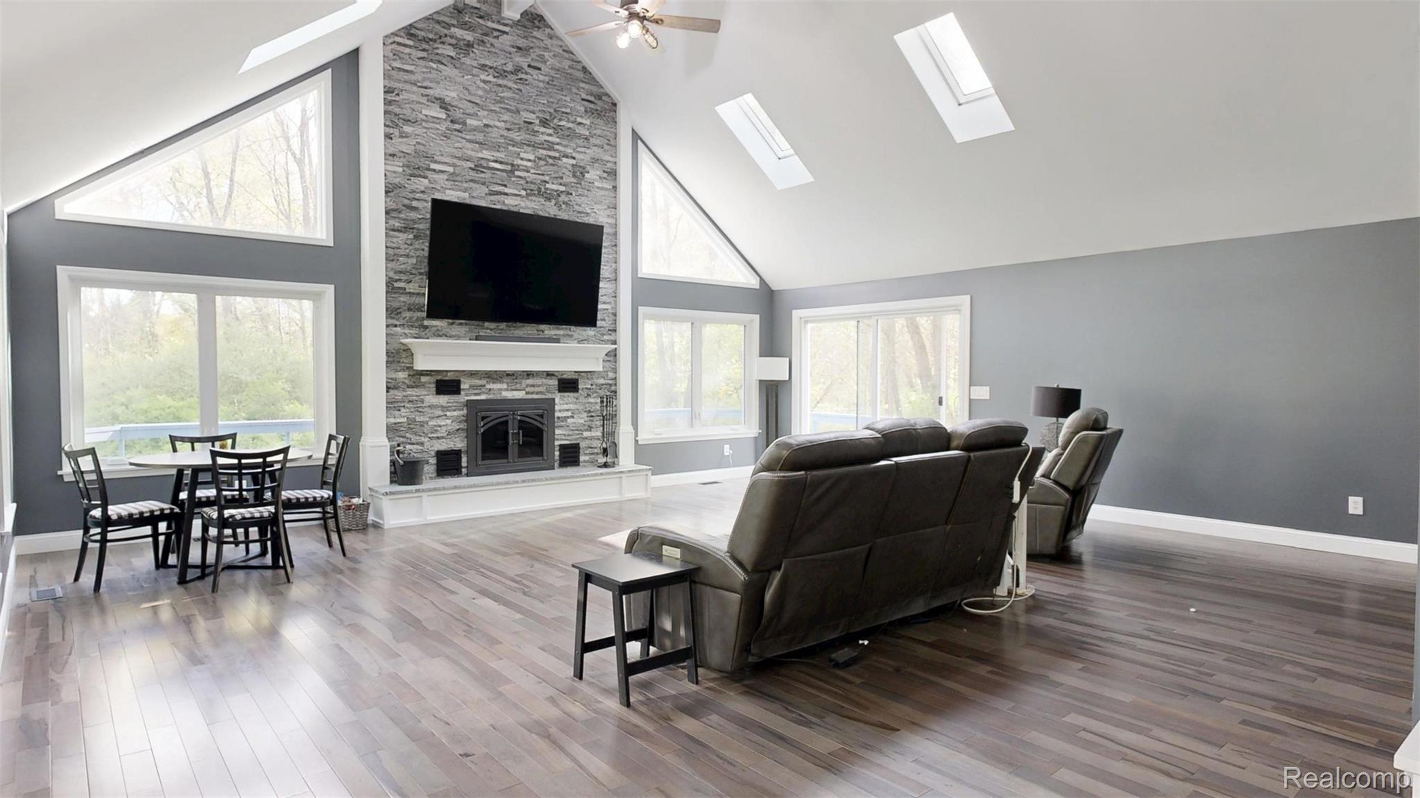 10300 Clark Road Davisburg, MI 48350 - Photo 12 of 39 Living area featuring a high ceiling, ceiling fan, a stone fireplace, wood finished floors, and a skylight