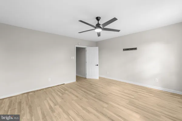 a view of an empty room with wooden floor and a ceiling fan