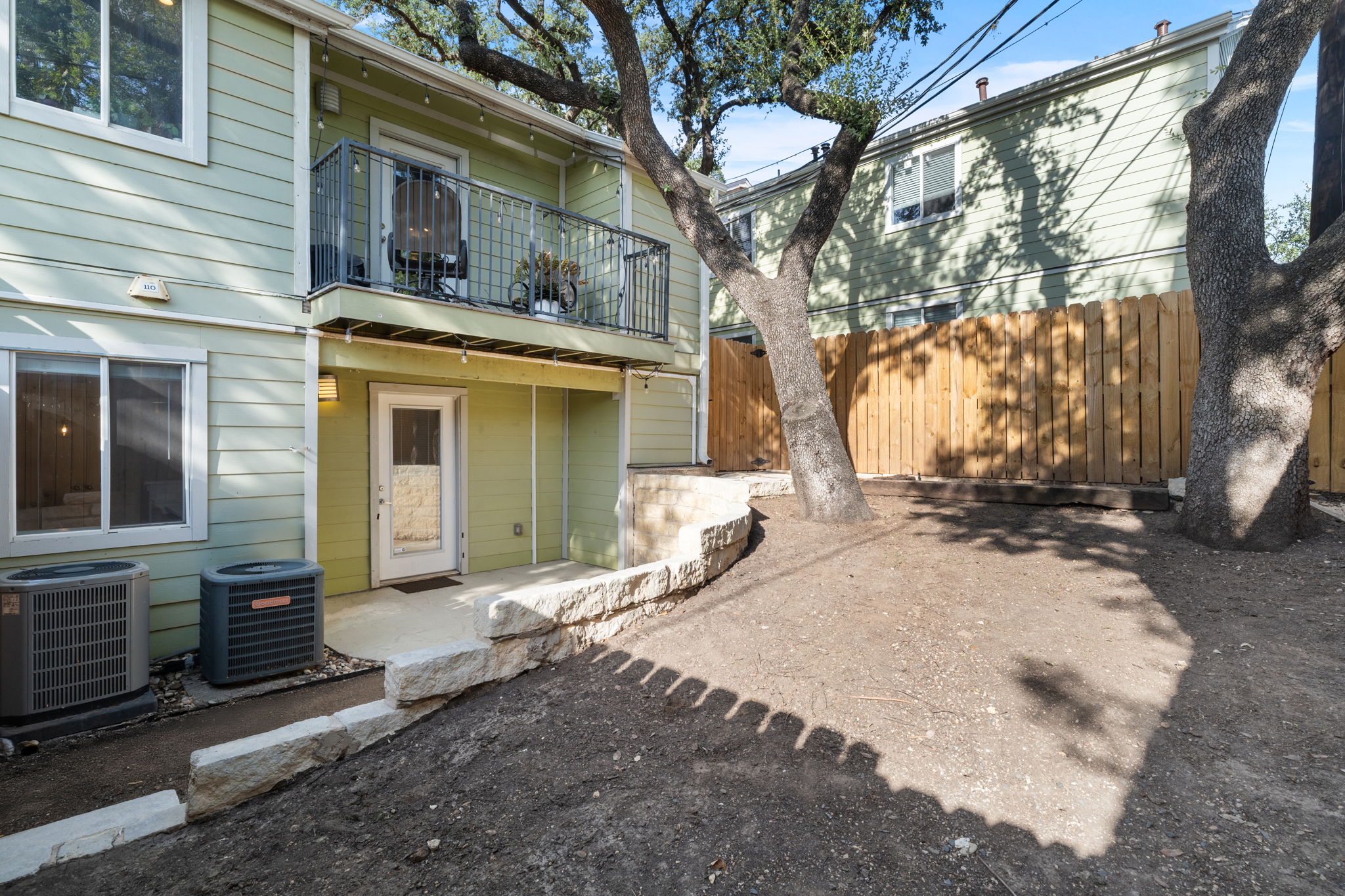 3601 Menchaca Road, Unit 110 Austin, TX 78704 - Photo 33 of 37 A well-maintained multi-level structure features a charming balcony overlooking a fenced yard with mature trees.