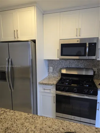 a kitchen with granite countertop a refrigerator and a stove top oven