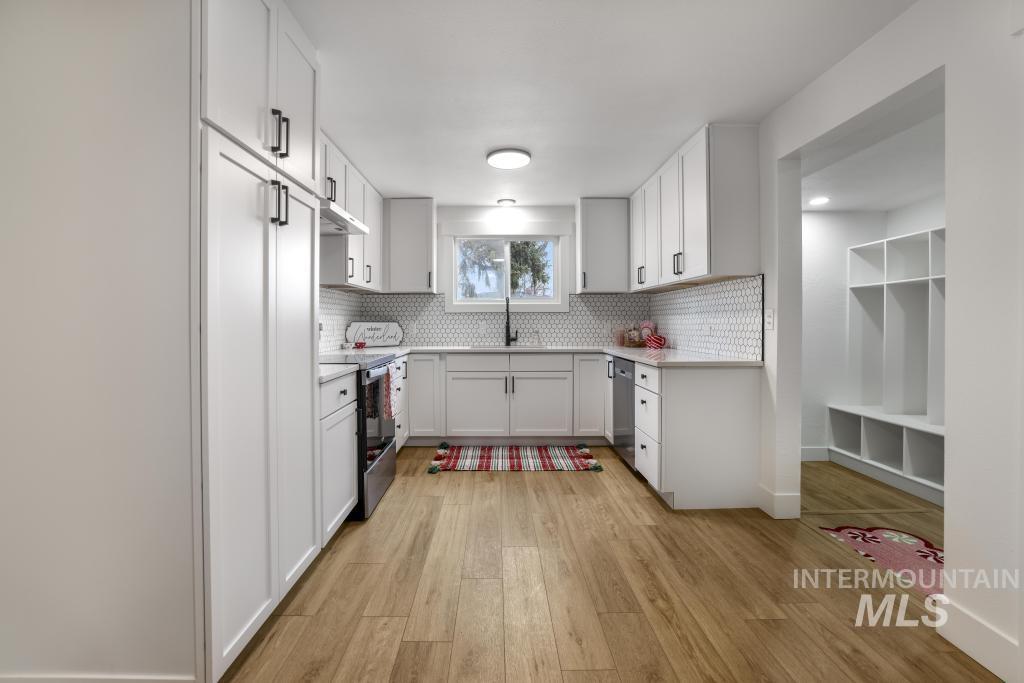 344 Fillmore Street Twin Falls, ID 83301 - Photo 11 of 42 Kitchen featuring light wood-type flooring, tasteful backsplash, stainless steel appliances, white cabinets, and under cabinet range hood