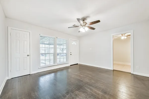 an empty room with wooden floor fan and windows