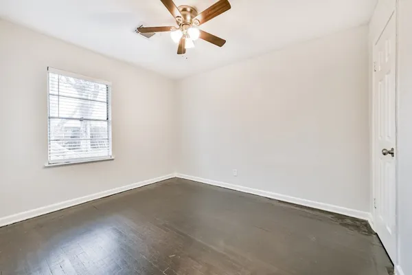 an empty room with wooden floor fan and windows