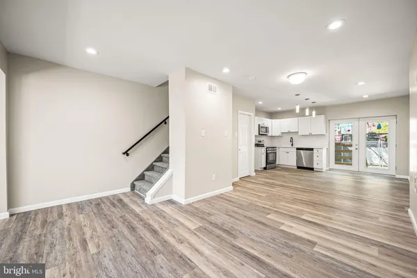 a view of an empty room with wooden floor and a kitchen