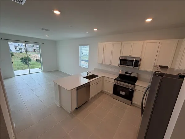 a kitchen with stainless steel appliances a stove a refrigerator a sink and white cabinets with wooden floor