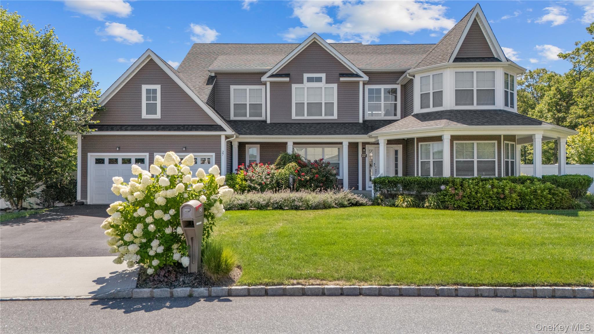 View of front facade featuring a front lawn, a porch, a shingled roof, driveway, and a garage