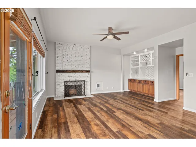 a view of an empty room with wooden floor fireplace and a window