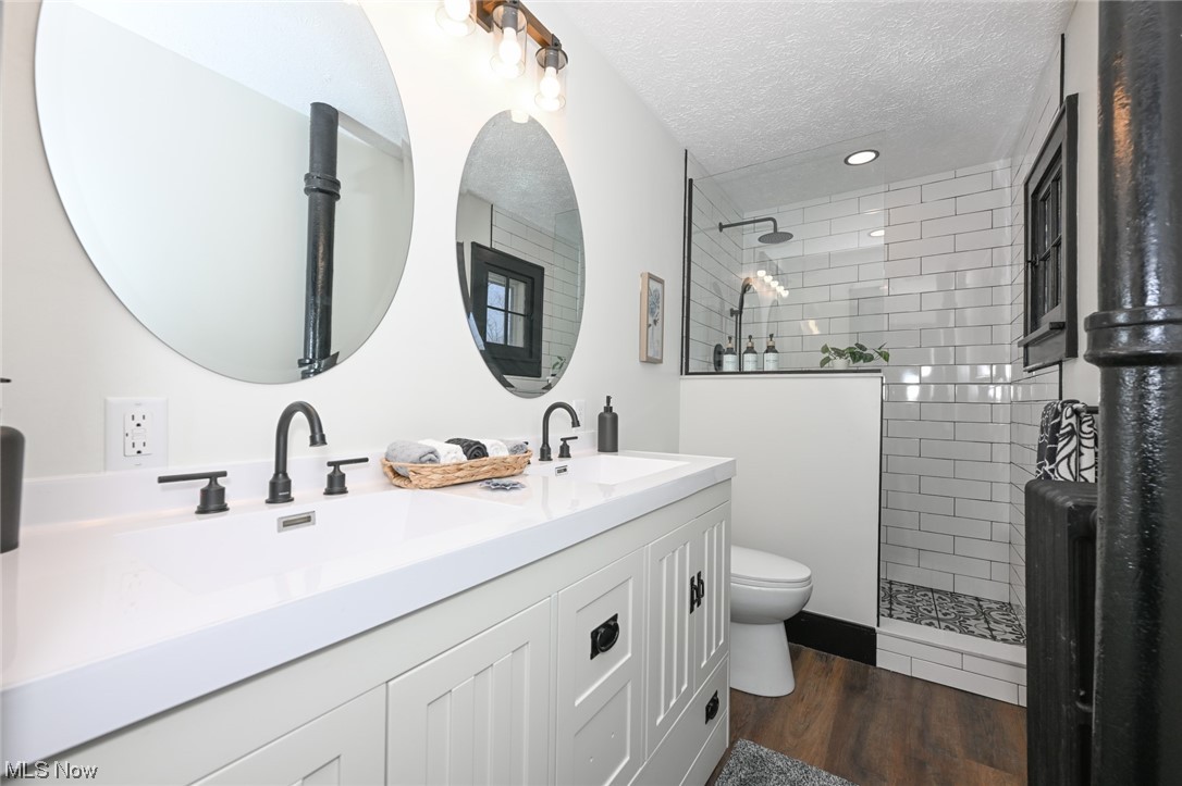 232 Randolph Road Mogadore, OH 44260 - Photo 19 of 35 Bathroom featuring double vanity, a textured ceiling, toilet, hardwood / wood-style flooring, and a tile shower