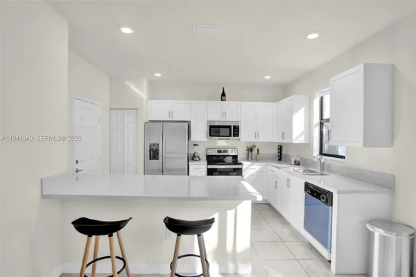 a large white kitchen with stainless steel appliances kitchen island granite countertop a sink and cabinets