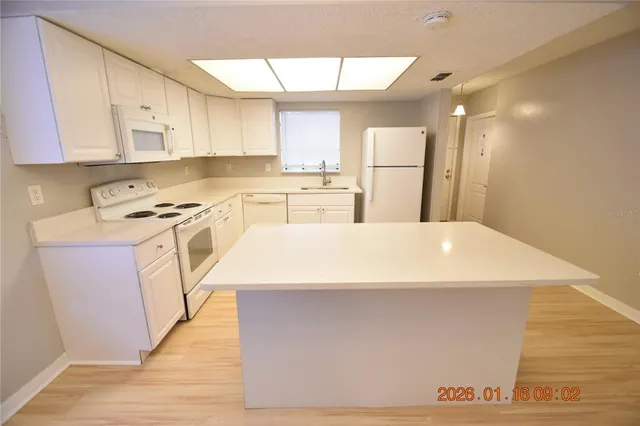 a kitchen with stainless steel appliances a stove top oven a sink a refrigerator white cabinets and wooden floor