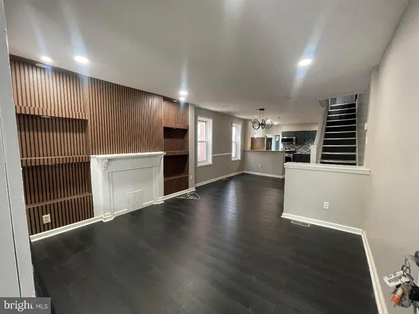 an empty room with wooden floor kitchen view and windows