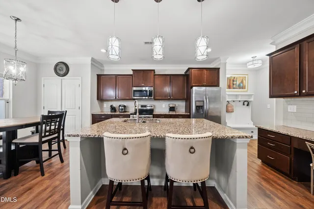 a kitchen with stainless steel appliances granite countertop a sink a stove a refrigerator cabinets and chairs