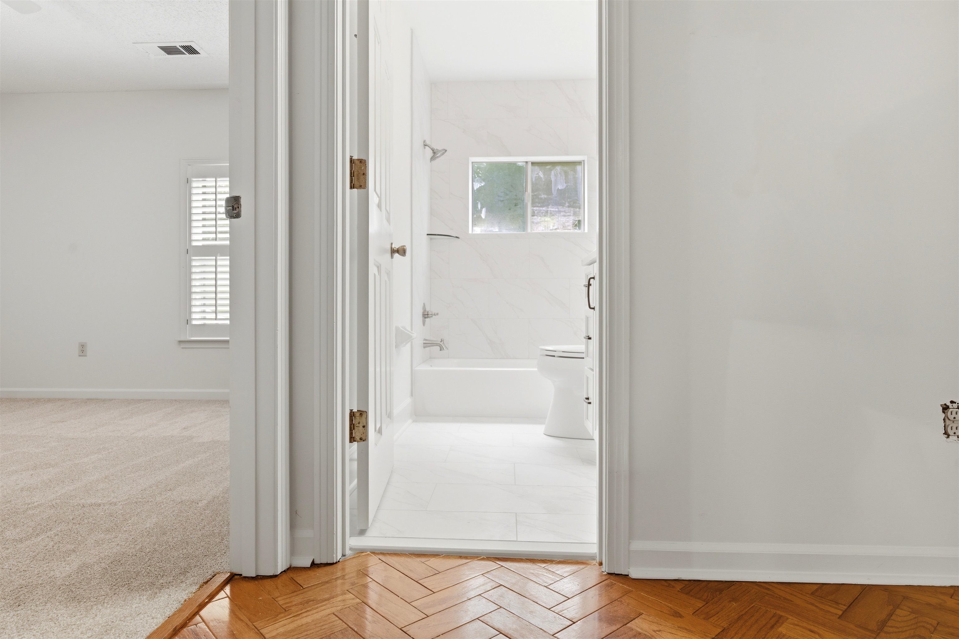 1984 Allenby Road Germantown, TN 38139 - Photo 29 of 37 Herringbone wood-finish flooring transitions to a white-tiled bathroom featuring a bathtub with a shower, a toilet, a window, and white wall tiling