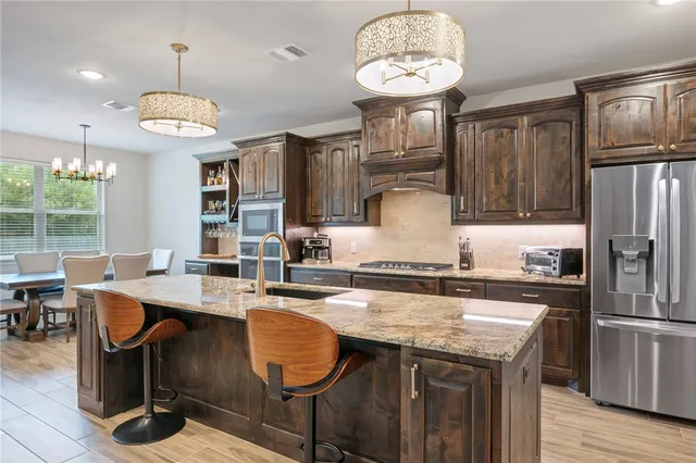 a kitchen with granite countertop a stove a refrigerator a sink dishwasher a dining table and chairs with wooden floor