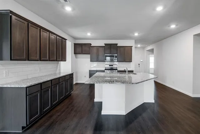 a kitchen with kitchen island granite countertop wooden cabinets a sink and a stove with wooden floor