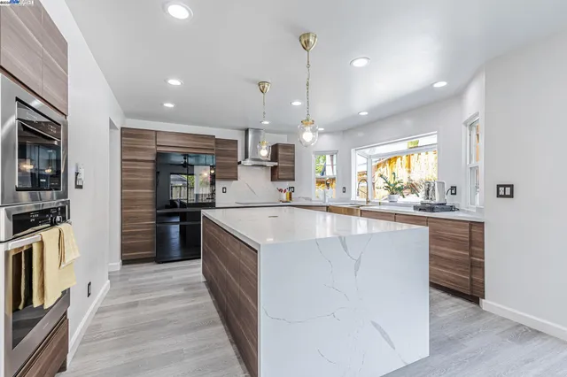 a large kitchen with stainless steel appliances kitchen island granite countertop a large counter top a stove a chimney a sink and a refrigerator