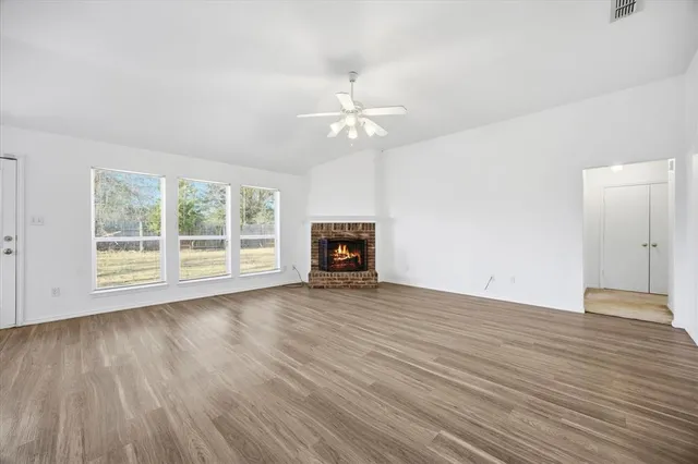 an empty room with wooden floor chandelier fan and windows