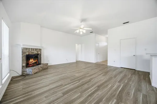 an empty room with wooden floor fireplace and windows