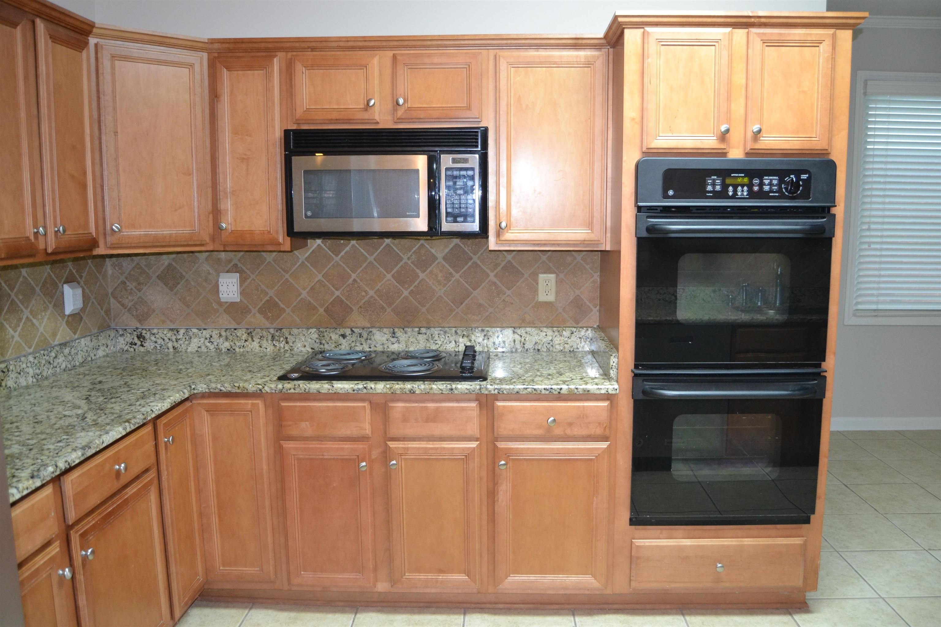 10486 Juneau Way Collierville, TN 38017 - Photo 19 of 33 Kitchen featuring decorative backsplash, light stone counters, crown molding, black appliances, and light tile patterned flooring