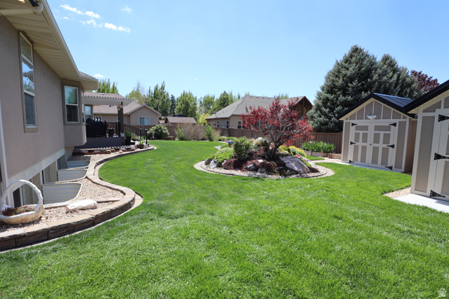 1055 North 1000 East Mapleton, UT 84664 - Photo 103 of 112 Expansive green lawn featuring a central rock garden with a red-leafed tree, a raised deck with a pergola, and two detached storage sheds