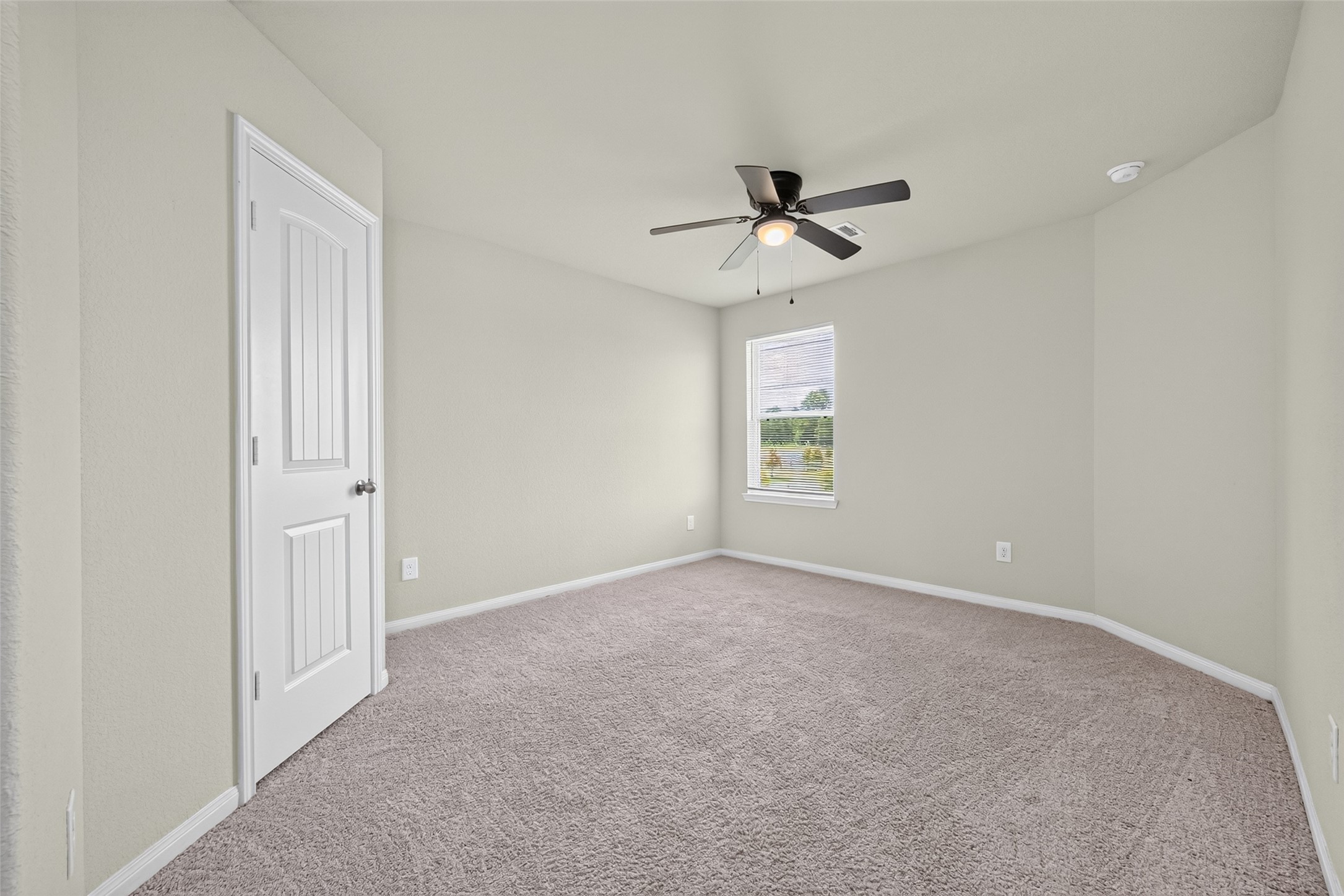 2526 Sturgeon Way Conroe, TX 77384 - Photo 32 of 49 This photo shows a bright bedroom with neutral walls and carpet, featuring a ceiling fan and a window that lets in natural light. A white door is visible, leading to an adjacent space.