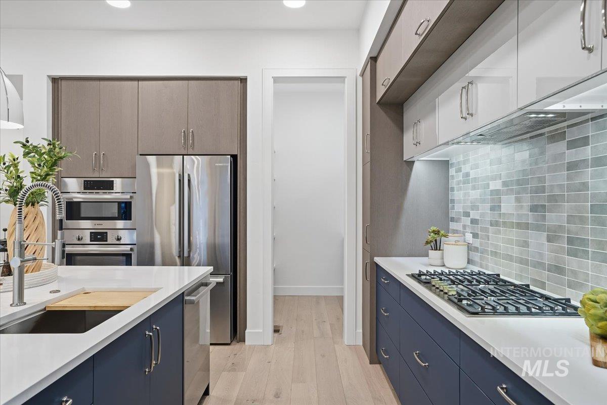 11717 North Rabbitbrush Way Boise, ID 83714 - Photo 14 of 33 Kitchen featuring backsplash, stainless steel appliances, light wood finished floors, blue cabinets, and light stone countertops