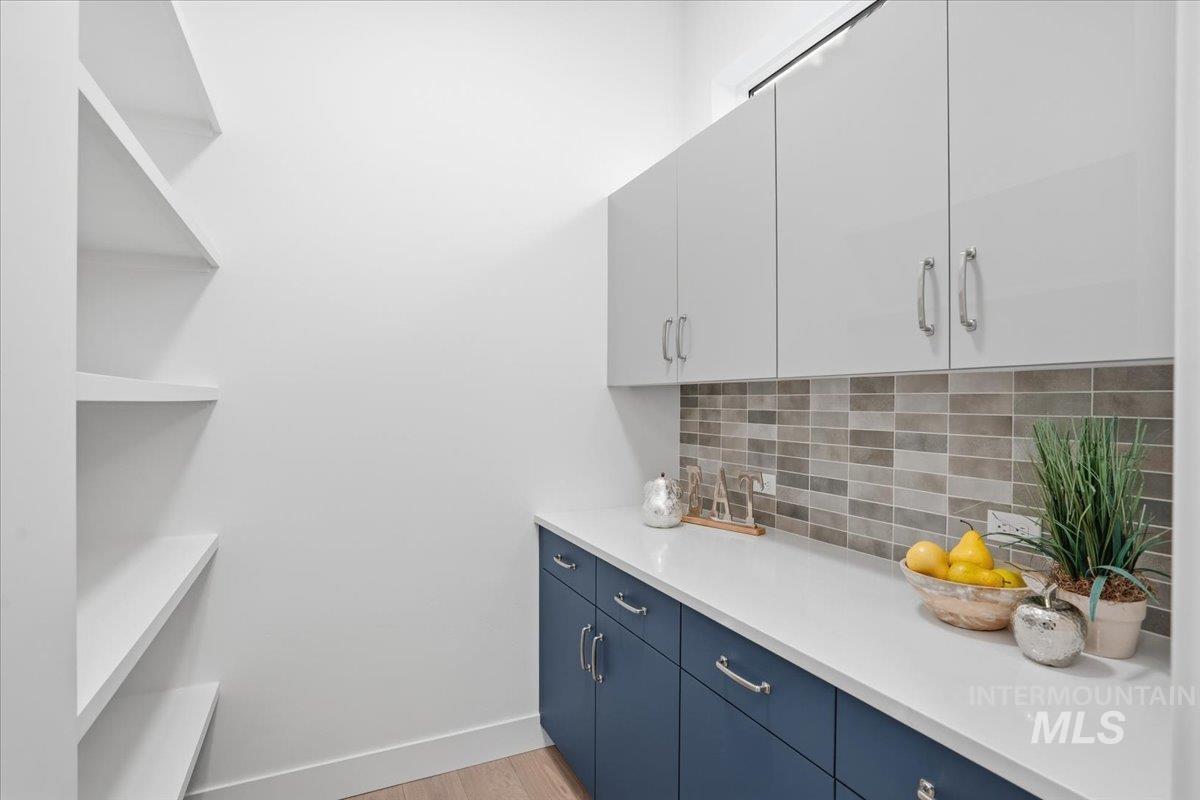 11717 North Rabbitbrush Way Boise, ID 83714 - Photo 18 of 33 Bar area featuring decorative backsplash, blue cabinetry, light wood finished floors, and white cabinets