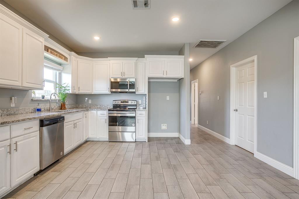 3901 Baylor Street Fort Worth, TX 76119 - Photo 18 of 40 a kitchen with granite countertop a refrigerator oven a sink dishwasher and white cabinets with wooden floor