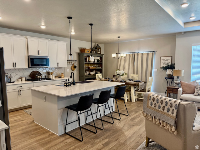 315 South Sherman Street Mapleton, UT 84664 - Photo 10 of 30 Open-concept kitchen featuring an island with integrated sink, white cabinetry with dark hardware, a tile backsplash, and stainless steel appliances