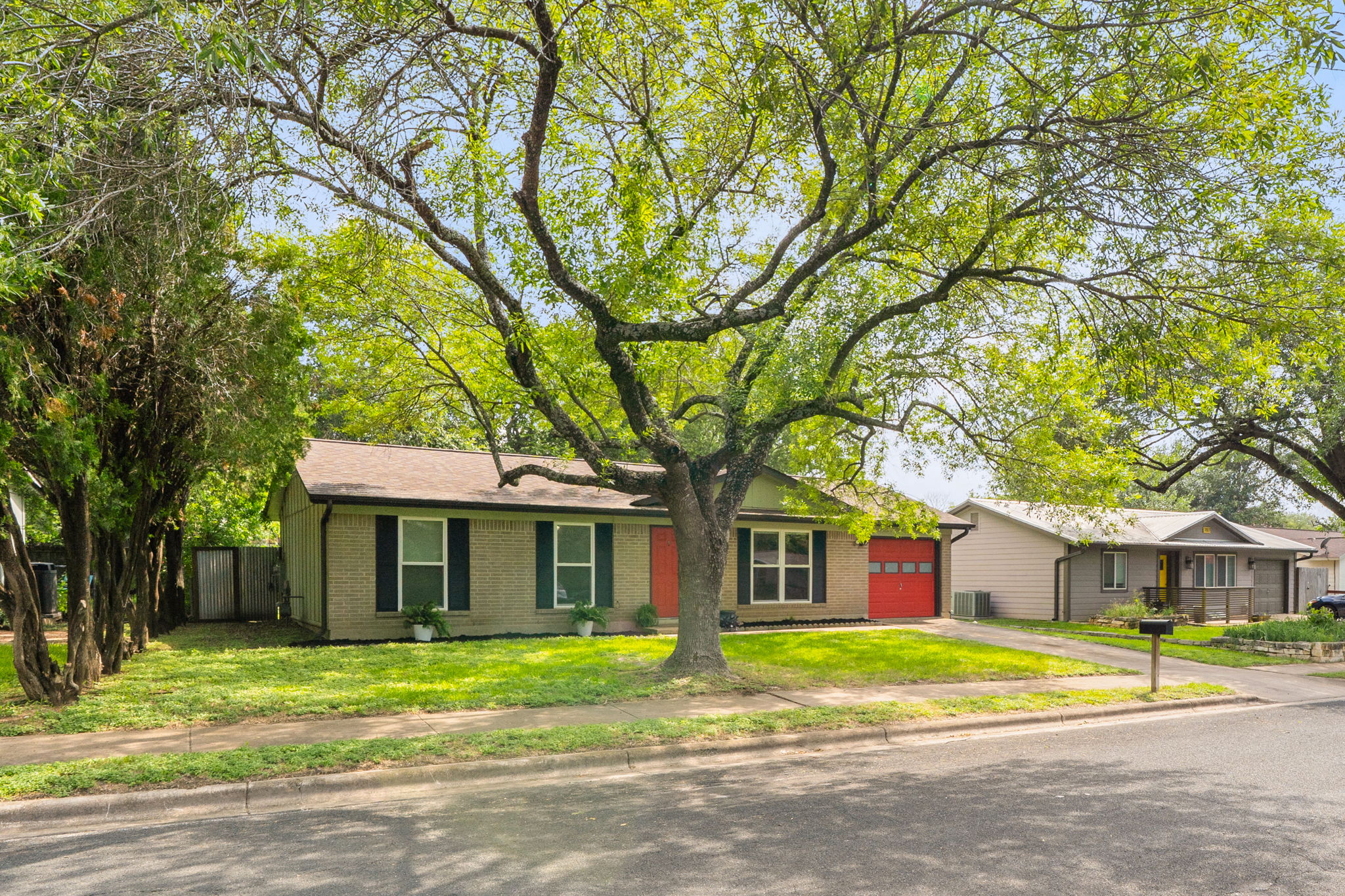 705 Dulwich Street Austin, TX 78748 - Photo 34 of 36 A well-maintained ranch-style home features a vibrant red garage door and lush front landscaping.
