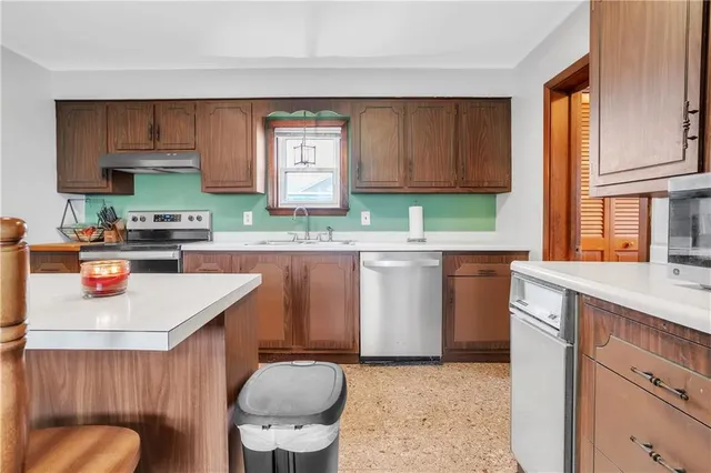 a kitchen with stainless steel appliances a sink a stove a refrigerator cabinets and a window