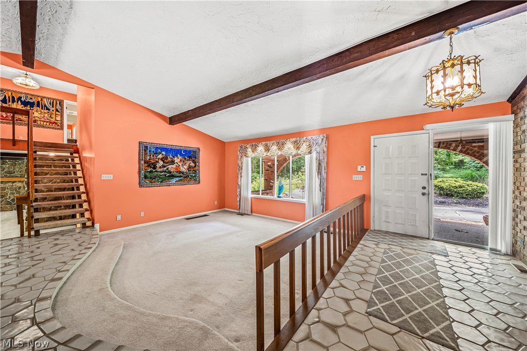 12200 Caves Road Chesterland, OH 44026 - Photo 9 of 43 Carpeted foyer entrance with lofted ceiling with beams and an inviting chandelier