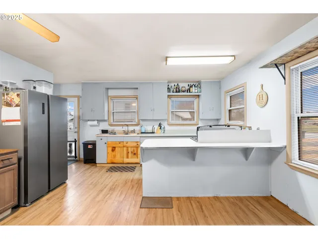 a living room with stainless steel appliances kitchen island granite countertop a refrigerator a stove a sink dishwasher and wooden cabinets with wooden floor