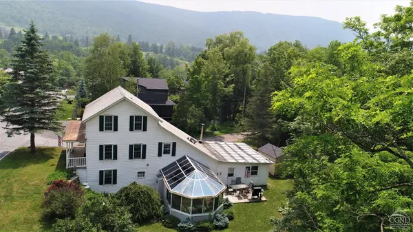 a view of a white house with a big yard plants and large trees